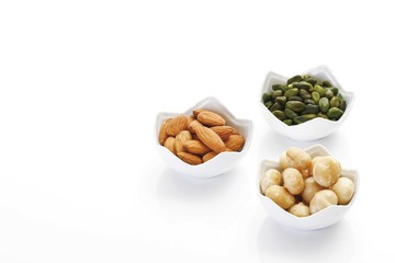 Assorted nuts in porcelain bowls, macadamia kernels, pistachio kernels and almond kernels