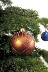 Copper Christmas ball ornament hanging from the branch of a Christmas tree
