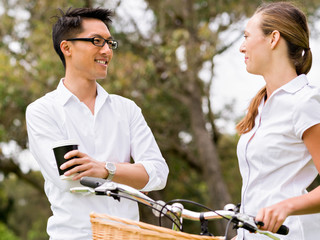 Portrait of smiling couple standing in park with bike talking