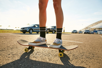 Legs of a girl standing on a skateboard on a parking in sunset - static