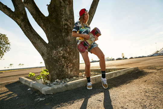 Skateboarder girl posing at sunset playing on her skateboard like a guitar