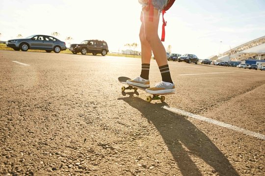 Legs of a girl standing on a skateboard on a parking in sunset - dinamic