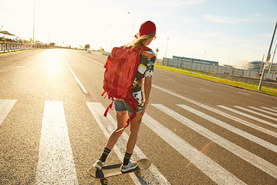 A skateboard girl crossing the road on zebra in the sun