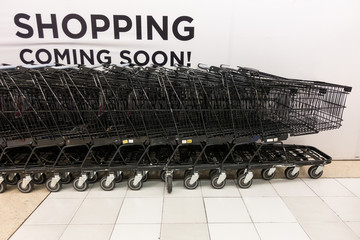 Black metal grocery shopping carts against white wall with shopping sign on white wall.