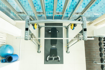 Fitness background with dumbells rack with black dumbells, press bench visible.