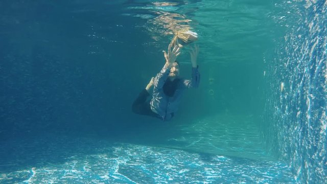 Man in suit tries to catch the book under water