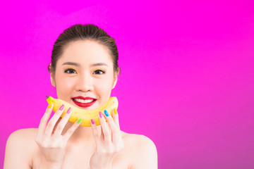 Young Asian woman holding banana isolated in pink background.