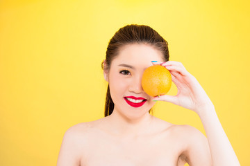 Obraz na płótnie Canvas Young Asian woman holding orange isolated in yellow background.