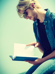 Sitting man reading book outside on sunny day