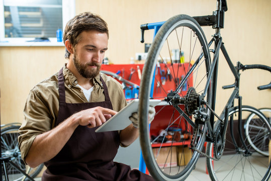 Contemporary repairman with tablet searching for necessary details for bicycle wheels in the net