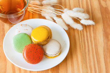 Colorful French macaron or Italian macaron on white plate. Homemade delicious macaron and tea on wood table with copy space for background or wallpaper. Macaron is popular dessert for served with tea.