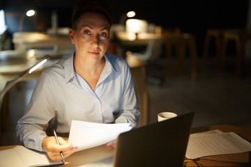 Middle-aged businesswoman with papers working overtime in office