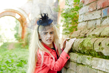 Blond girl in red jacket and black retro hat standing by corner of brick house