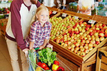 Young man riding his daughter on shopping cart while buying food in supermarket