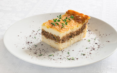 cut-off pastitsio piece on plate with thyme and sumac