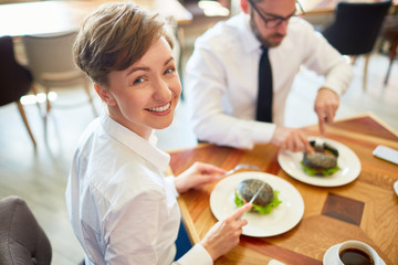 Happy businesswoman sitting by table and having snack at lunch with colleague