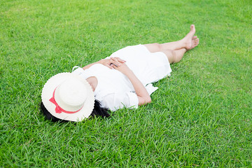  Happy woman lying on green grass meadow on top of mountain edge cliff enjoying sun on her face.Relaxing concept