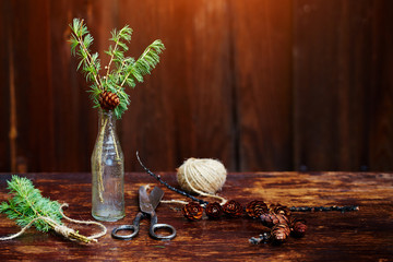Christmas wooden background.Spruce branches and cones in a vintage bottle, the old scissors and crafty cord. The concept of training sets for Christmas.