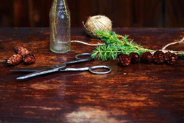 Christmas wooden background.Spruce branches and cones in a vintage bottle, the old scissors and crafty cord. The concept of training sets for Christmas.