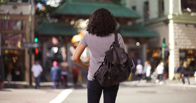 Rear view of cute black female sightseeing in Chinatown, taking photo with phone