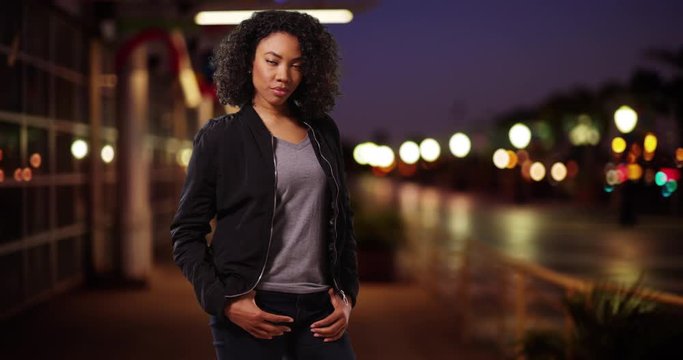 Cute black woman on urban street at night looking at camera with cool confidence