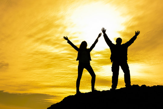 Two people between clouds Full length silhouette of happy couple stand together on peak of a mountain with hands raised up, sunset and ocean. Man and woman on top mountain look at beautiful night