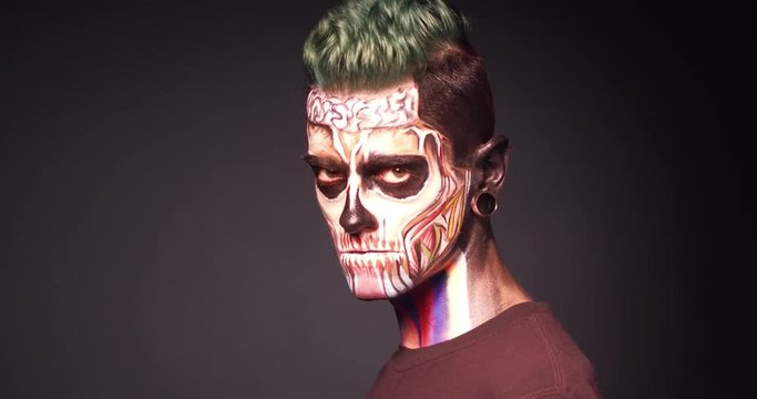 Man with Halloween skull make up in studio. Light and shadow footage of man with scary skeleton face.
