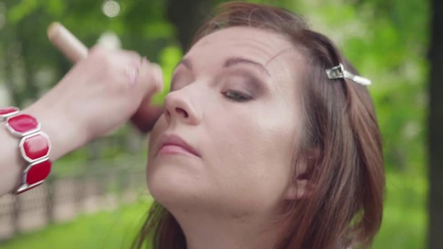 Make up artist harmonises girl's face complexion before photoshoot and applies eyeshadows on lid