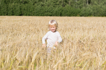 Blond Slavic happy kid boy at a ripe rye wheat field, autumn harvest, Russian forest, the Urals