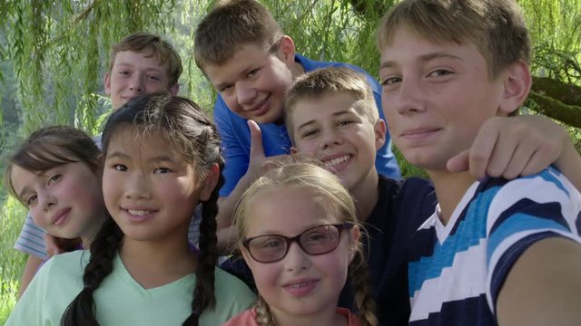 Group of boys and girls pose for a self-taken photograph under a tree while at outdoor summer camp. Hand-held slow motion 4K recorded at 60fps