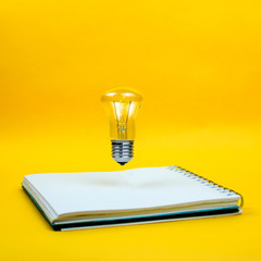 Light bulb levitating above the notebook as a concept of new idea, square, copyspace, yellow...