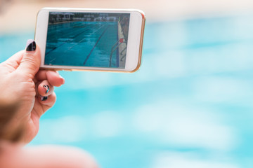 woman hand holding her phone recording swimming pool activities