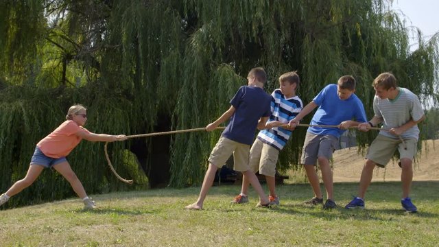 Young girl takes on four boys at tug of war match and pulls them over, walks over and celebrates. Hand-held slow motion 4K recorded at 60fps.