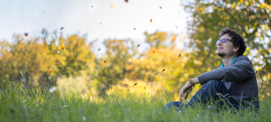 Junger Mann sitzt im Gras, tanzende Blätter, Textfreiraum, Breitbild