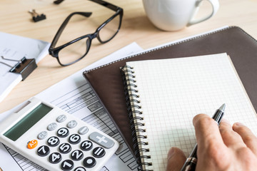 Close up young man hand using calculator and writing make note on desk office