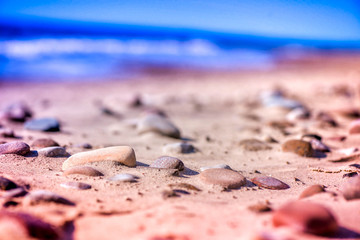 Macro shot of magical, healing, warm sea pebbles, stones and rocks, laying on beach sand. Ocean waves background in summer evening, during the sunset. Calm, relaxing walk on seaside. Perfect vacation.
