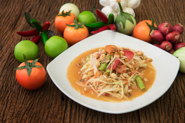  Thai food ingredients to make Som Tum (or Papaya salad) : grated papaya, cherry tomatoes, red hot peppers, lemon and garlic. Papaya salad on white dish on wood background.