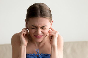 Young annoyed woman sticking fingers in ears with eyes closed, not listening to loud noise, ignoring stressful environment, stubborn teen refuses hearing, feels ear ache, tinnitus, head shot portrait