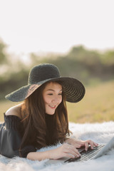 Portrait of happy Asian woman  lying on the grass using her laptop. Business woman working online.