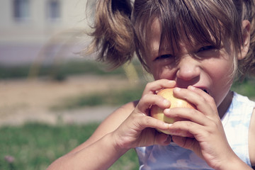 Girl with tails gnawing apples in the street on a hot sunny day.