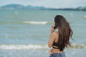 Back view image of young woman standing at beach and talking by her phone. Concept good signal.