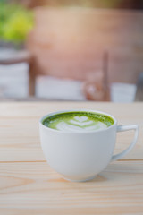  cup of green tea on wooden tray with pine cones and water on table.