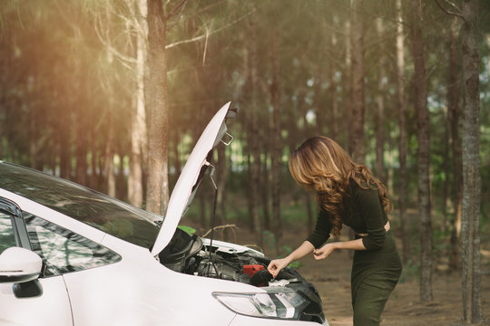 Portrait of asian woman  on the road trying to fix their car over pine tree background. Vintage tone with sunlight effect picture.