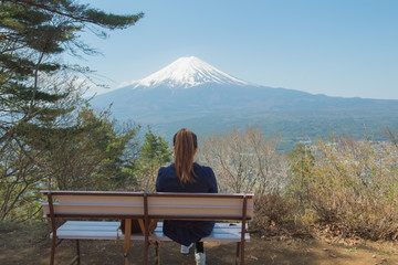 Naklejka na ściany i meble Young asian tourist sit down on top of a mountain and enjoying morning mountain Fuji view. asian woman sit down at cliff at mountain Fuji in japan