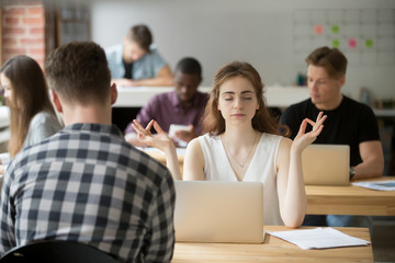 Calm businesswoman meditating in yoga pose in modern office setting. Business lady taking care of her health during break. Reducing discomfort at workplace, staying in focus, stress relief at work.