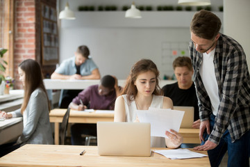 Young female entrepreneur holds paperwork, explains information in documents to coworker. Job supervisor tells male employee specifics of workflow, approving business report, verifying work strategy.