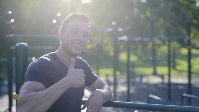 Smiling athlete young man gesturing thumb up and smiling on sports playground