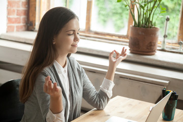 Calm businesswoman meditating in yoga pose in modern office setting. Business lady taking care of her health during break. Reducing discomfort at workplace, staying in focus, stress relief at work.