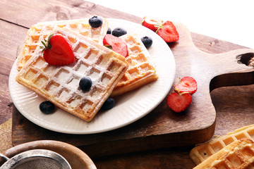 Homemade waffles with berries in plate on wooden table