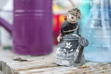 Quirky ornamental children’s character riding on a rustic flower decorated watering can in a traditional English potting shed or green house